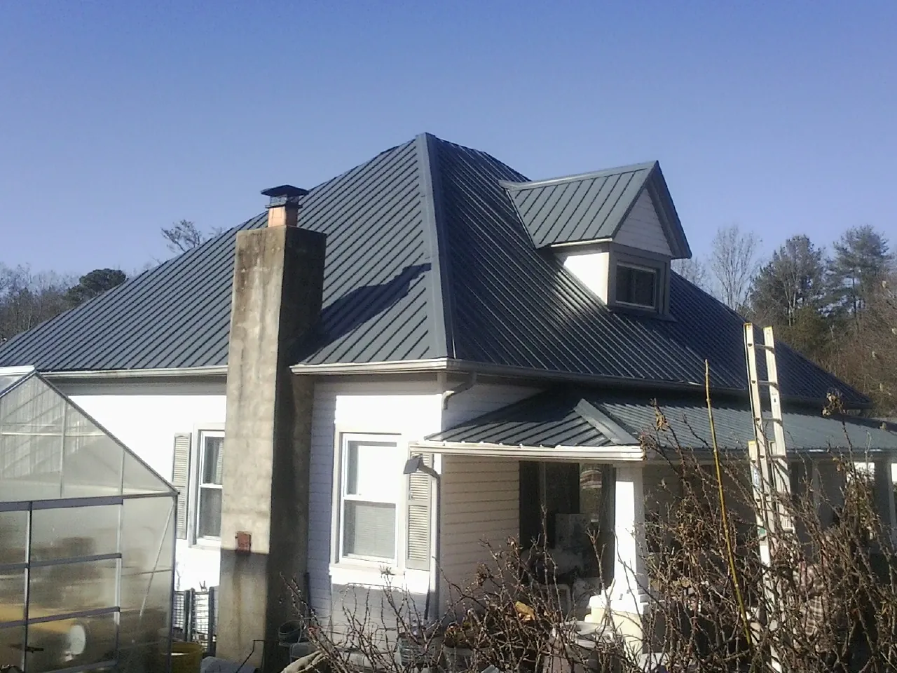 Dark blue standing seam metal roof on a white farmhouse with dormer — Slate & Tile Roof Repair by Roofing Brothers in Boonton