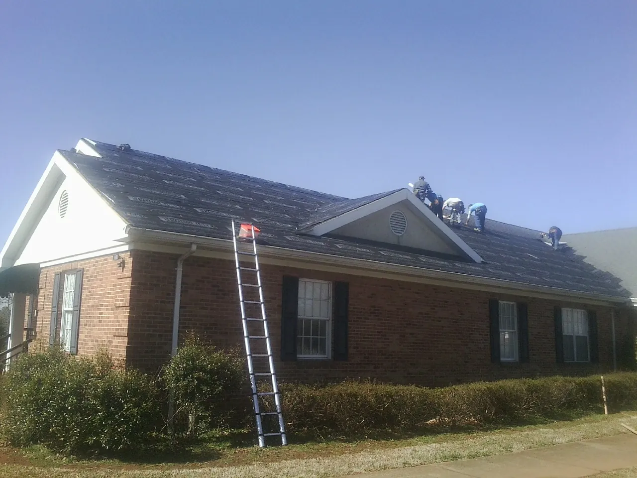 Crew tearing shingles off a brick ranch roof with a ladder set — Metal Roof Repair work by our crew in Boonton