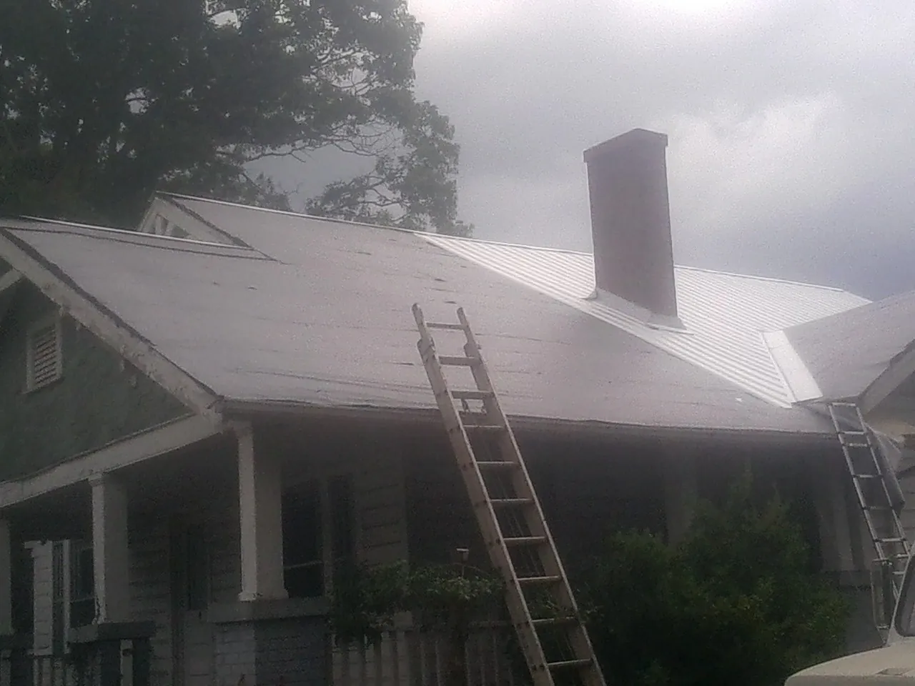 Ladders against a metal roof on an older home with a brick chimney in Boonton