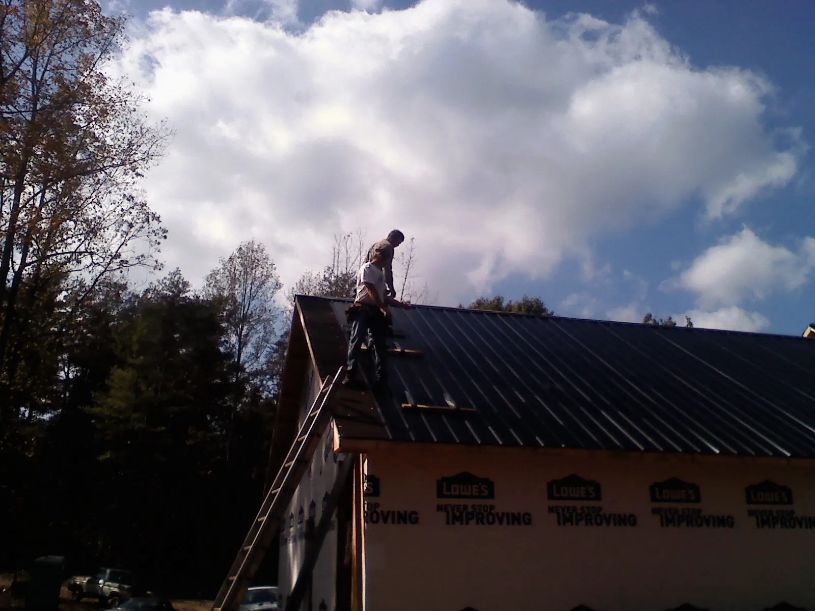 Roofer fastening dark metal panels high against a cloudy sky, from a Roof Inspection job in Boonton