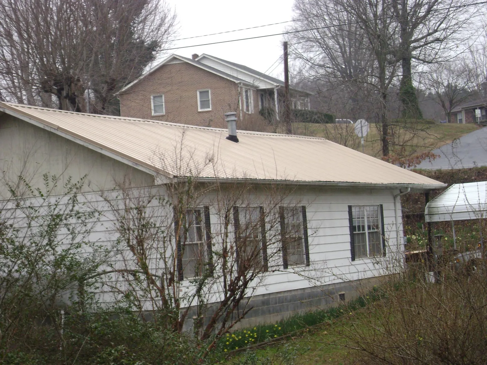 Tan metal roof on a white sided house set into a hillside — Commercial Roofing by Roofing Brothers in Boonton